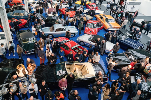 A used car auction, lots of people inspecting cars going to auction